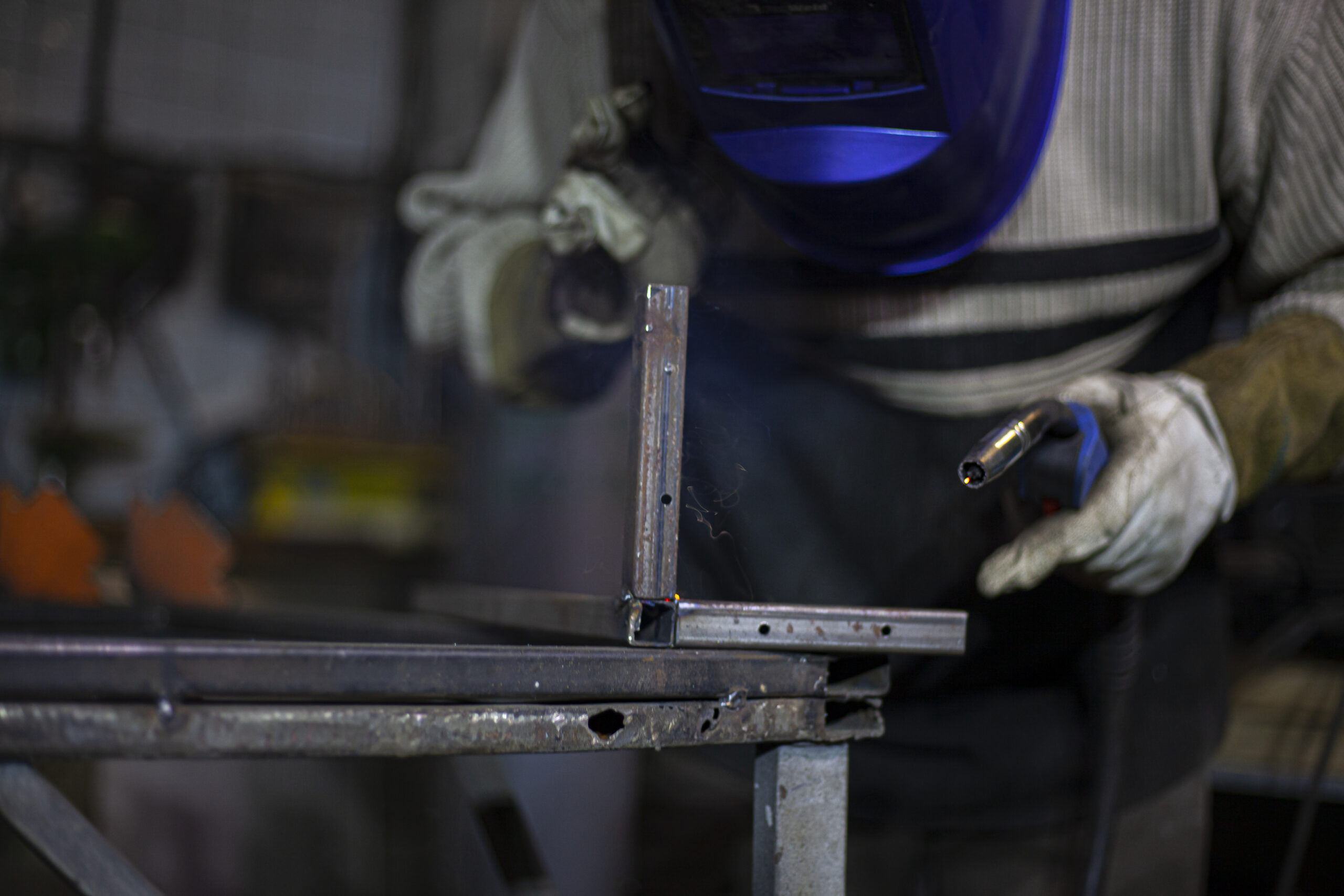 Welder at work. The welder heats the metal. Classes in the workshop. Steel processing. Welder in a blue welding mask. High melting point of metal. A man doing hard work.